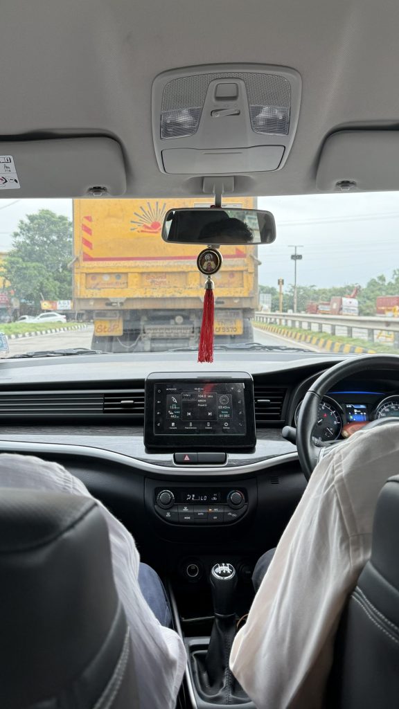Vue depuis l'habitacle d'une voiture, avec klaxon visible sur le volant, suivant un camion jaune sur la route.