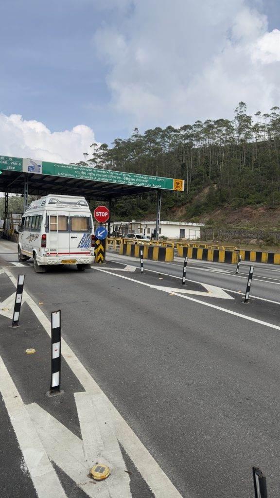 Minibus passant un poste de péage sur une autoroute entourée de collines boisées.