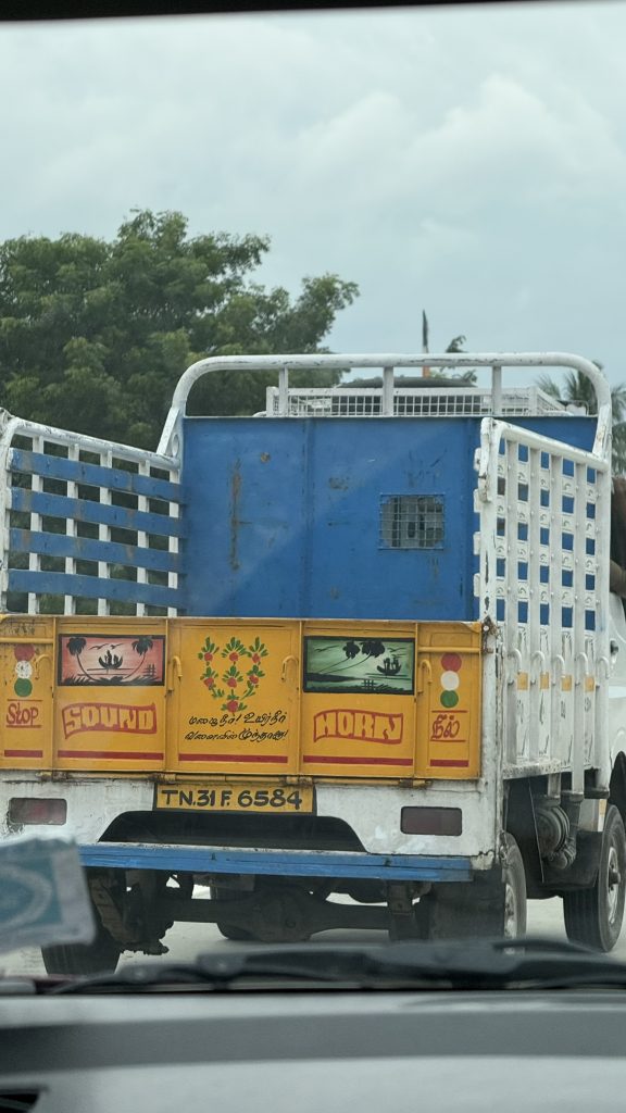 Camion coloré sur une route, avec des panneaux jaunes et bleus portant des inscriptions décoratives.